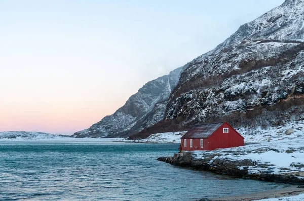 北極の険しい山々や雪に覆われたビーチに囲まれた伝統的なノルウェーの赤い納屋 武道の町の近くに太陽の短い期間の黄金の時間の間に表示されます — ストック写真