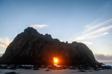 Pfeiffer Sahili, Kaliforniya 'daki anahtar deliği kemerinin geniş açılı görüntüsü, batan güneşi merkez delikten gözetliyor. Kaliforniya 'da bir kış akşamında gün batımı.