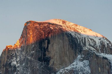 Batan güneşin son ışığı kış öğleden sonra karla kaplı yarım bir kubbeyi aydınlatıyor. Yosemite Milli Parkı.