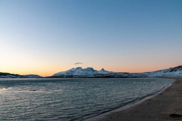 鮮やかなオレンジ色の輝きは Bodoの町の近くにある北極の北西部の険しい山々や雪に覆われたビーチの劇的な背景として機能する黄金の時間の空を彩ります — ストック写真