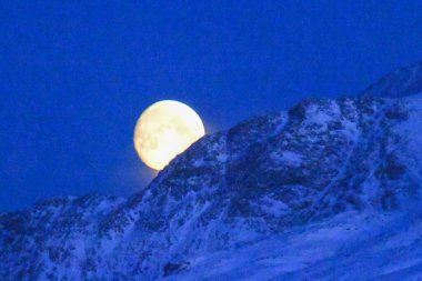 A near full moon is slowly creeping behind a mountain along the norwegian coast on an early winter morning near the town of Bodo.