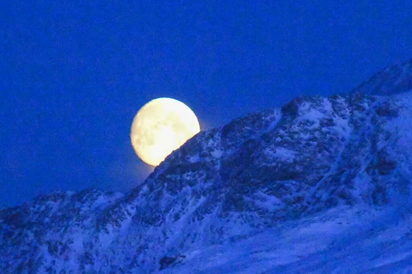 stock image A near full moon is slowly creeping behind a mountain along the norwegian coast on an early winter morning near the town of Bodo.