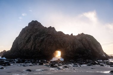 Pfeiffer Sahili, Kaliforniya 'daki anahtar deliği kemerinin geniş açılı görüntüsü, batan güneşi merkez delikten gözetliyor. Kaliforniya 'da bir kış akşamında gün batımı.