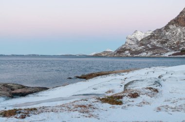 Landscape shot highlighting the rugged mountains and snow-covered beaches of arctic norway during a brief golden hour during the long winters.