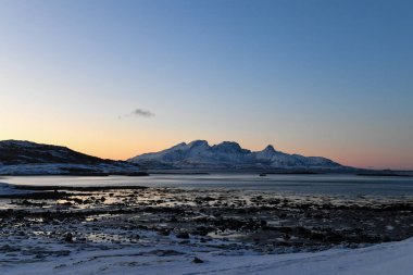 Wide angle landscape shot of the snow covered mountains and beach near Mjelle, part of the Bodo community in Arctic Norway, during the brief period of daylight in the arctic winter.