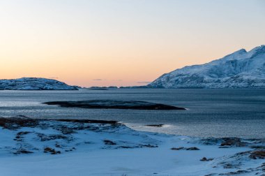 Landscape shot highlighting the rugged mountains and snow-covered beaches of arctic norway during a brief golden hour during the long winters.