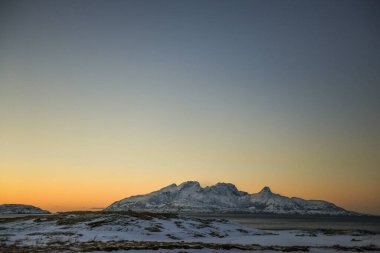 Landscape shot highlighting the rugged mountains and snow-covered beaches of arctic norway during a brief golden hour during the long winters.
