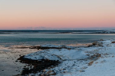 Landscape shot highlighting the rugged mountains and snow-covered beaches of arctic norway during a brief golden hour during the long winters.