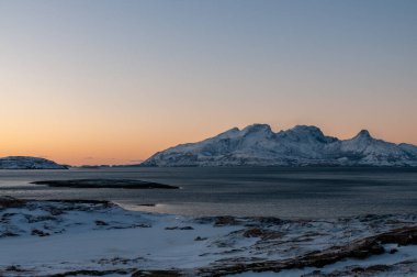 Landscape shot highlighting the rugged mountains and snow-covered beaches of arctic norway during a brief golden hour during the long winters.