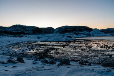 Wide angle landscape shot of the snow covered mountains and beach near Mjelle, part of the Bodo community in Arctic Norway, during the brief period of daylight in the arctic winter. clipart
