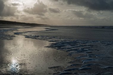 Hollanda, Kuzey Hollanda 'da Egmond aan Zeen yakınlarındaki sahilde bir su kalıntısına yansıyan bulutlar..