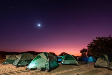 Bu sabahın erken saatlerinde Namibya 'nın güneyindeki bir kamp alanında bir grup çadırın aydınlatıldığı bir dolunay görüldü..