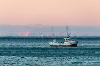 Bodo, Norveç - Ocak 04, 2023. Küçük bir balıkçı teknesi Atlantik Okyanusu 'nda demirlemiş ve arka planda lofotenin karla kaplı dağları var..