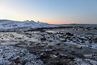 Wide angle shot of ice and boulders along the Norwegian coast, on a snowy winter morning. clipart