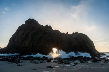 Pfeiffer Sahili, Kaliforniya 'daki anahtar deliği kemerinin geniş açılı görüntüsü, batan güneşi merkez delikten gözetliyor. Kaliforniya 'da bir kış akşamında gün batımı.
