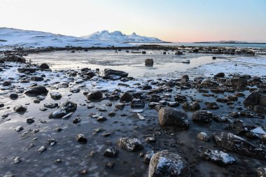 Wide angle shot of ice and boulders along the Norwegian coast, on a snowy winter morning.