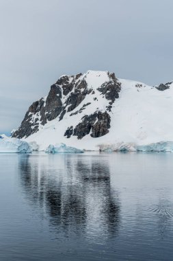 Antarktika Yarımadası 'nın engebeli dağlarının dikey çekimi ve sudaki yansımaları. Danco Adası, Antarktika