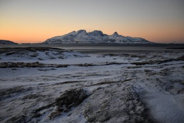 Landscape shot highlighting the rugged mountains and snow-covered beaches of arctic norway during a brief golden hour during the long winters.