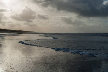 Hollanda, Kuzey Hollanda 'da Egmond aan Zeen yakınlarındaki sahilde bir su kalıntısına yansıyan bulutlar..