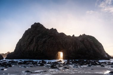 Pfeiffer Sahili, Kaliforniya 'daki anahtar deliği kemerinin geniş açılı görüntüsü, batan güneşi merkez delikten gözetliyor. Kaliforniya 'da bir kış akşamında gün batımı.