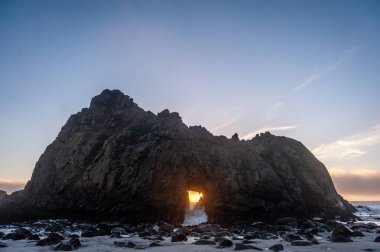 Pfeiffer Sahili, Kaliforniya 'daki anahtar deliği kemerinin geniş açılı görüntüsü, batan güneşi merkez delikten gözetliyor. Kaliforniya 'da bir kış akşamında gün batımı.