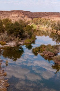 Alçak asılı bulutlar Namibya 'nın güneyindeki balık nehrinin suyuna yansıyor..