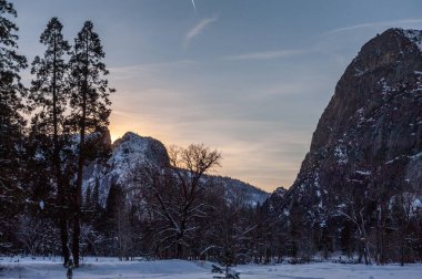 Yosemite Ulusal Parkı 'ndaki dağların arkasında batan güneş karla kaplı ağaçları aydınlatıyor..
