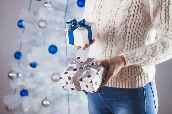 Unrecognizable woman in white sweater and jeans in front of Christmas tree with present