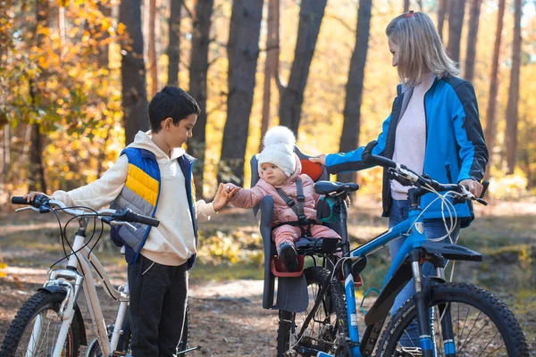 children with mom ride a bike one autumn day in a pine forest Family biking in the forest.