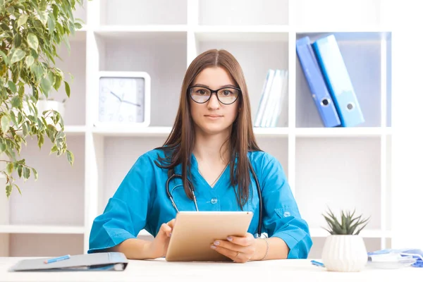 Young brunette woman doctor with laptop in a turquoise coat in a clinical office. Health care concept.