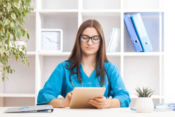 Young brunette woman doctor with laptop in a turquoise coat in a clinical office. Health care concept.