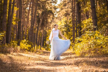 Çiçekli mutlu gelin yeşil parkta yürüyor.