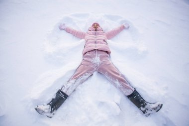 Karda uzanmış, kollarını ve bacaklarını aşağı yukarı hareket ettirerek bir kar meleği figürü oluşturan mutlu kadının yüksek açılı görüntüsü. Kış tatilinde karda uzanan gülümseyen kadın.