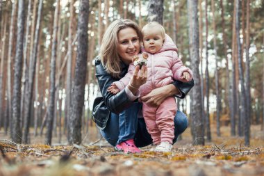 mom and little baby daughter are walking in a pine forest. mother carries her baby on her neck