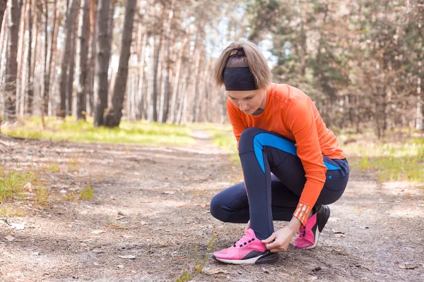 女跑步者把鞋带绑在运动鞋上 早上在森林里慢跑 — 图库照片