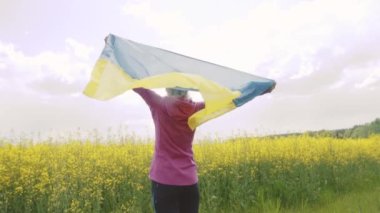 Tecavüz tarlasında Ukrayna bayrağı taşıyan genç bir kadın. Ulusal bayrak sallayarak barış için dua ediyor. Bağımsızlık Günü 'nü kutlayan mutlu kız.