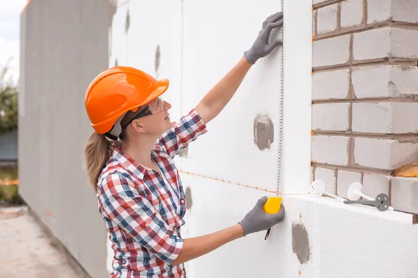 ポリフォームで家の断熱材 女性労働者は ファサードにポリスチレン板の設置の精度を建設レベルでチェックしています — ストック写真