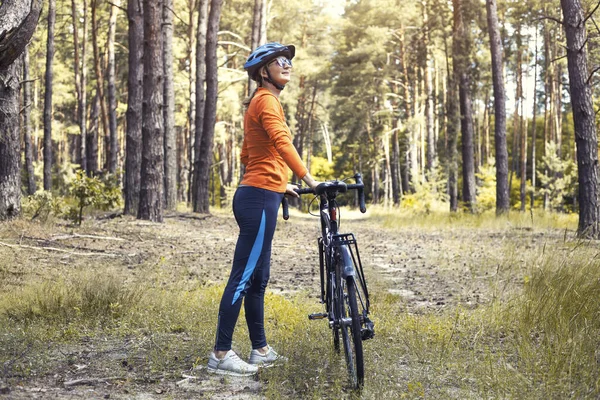 Happy woman cyclist, in a helmet, rides in the forest on a mountain bike. Adventure travel.