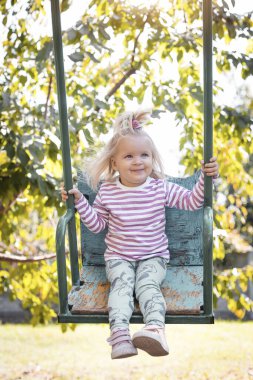 Küçük kız güzel bir yaz bahçesinde salıncakta sallanıyor. Çocuklar için aktif yaz tatili.