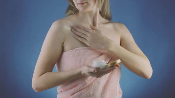青い背景のタオルの女性は彼女の肌に夕方のクリームを適用します ストック動画