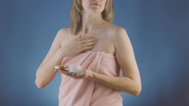 穿着蓝色背景毛巾的女人在皮肤上涂上晚霜 免版税图库视频