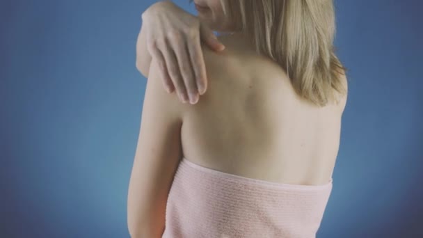 青い背景のタオルの女性は彼女の肌に夕方のクリームを適用します ロイヤリティフリーストック映像