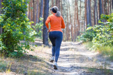 Güneşli bir çam ormanında sabah koşusunda olan genç bir kız. Kardiyo çalışması ve sağlıklı yaşam tarzı