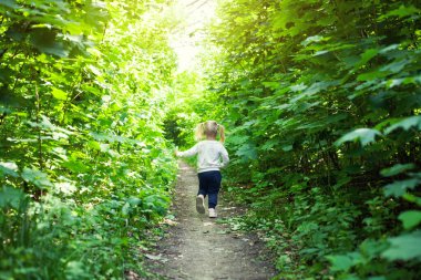 Gülümseyen kız yaprak döken ormanda yolda koşar. El sallıyor. Parlak ışık arkaplanındaki orman.