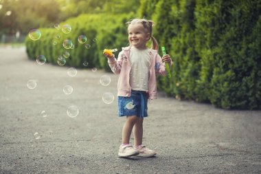 Parkta sabun köpüğü üfleyen küçük beyaz kız çocuğu. Mutlu tasasız çocukluk