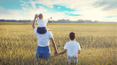 Aile yaz yürüyüşüne çıkıyor, anne ve çocuklar buğday tarlasında yürüyor ve gün batımında güzel doğanın tadını çıkarıyor.