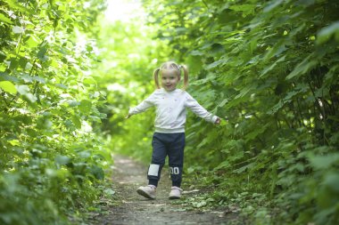Gülümseyen kız yaprak döken ormanda yolda koşar. El sallıyor. Parlak ışık arkaplanındaki orman.