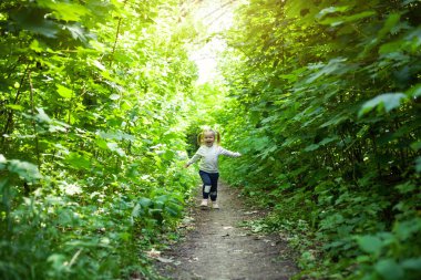 Gülümseyen kız yaprak döken ormanda yolda koşar. El sallıyor. Parlak ışık arkaplanındaki orman.