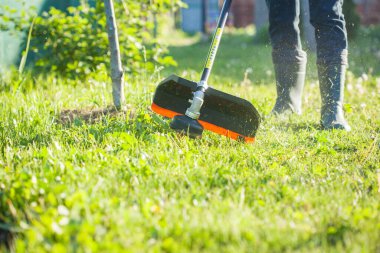 İşçi çimenleri el budayıcı ile biçiyor. Bahçe bakımı. Ot kontrolü. Çim biçme makinesi işçisi, bahçe işleri..