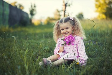 Köyün çayırında şakayıklı pembe elbiseli, örgülü, üç yaşında neşeli bir kız. Mutlu çocukluk